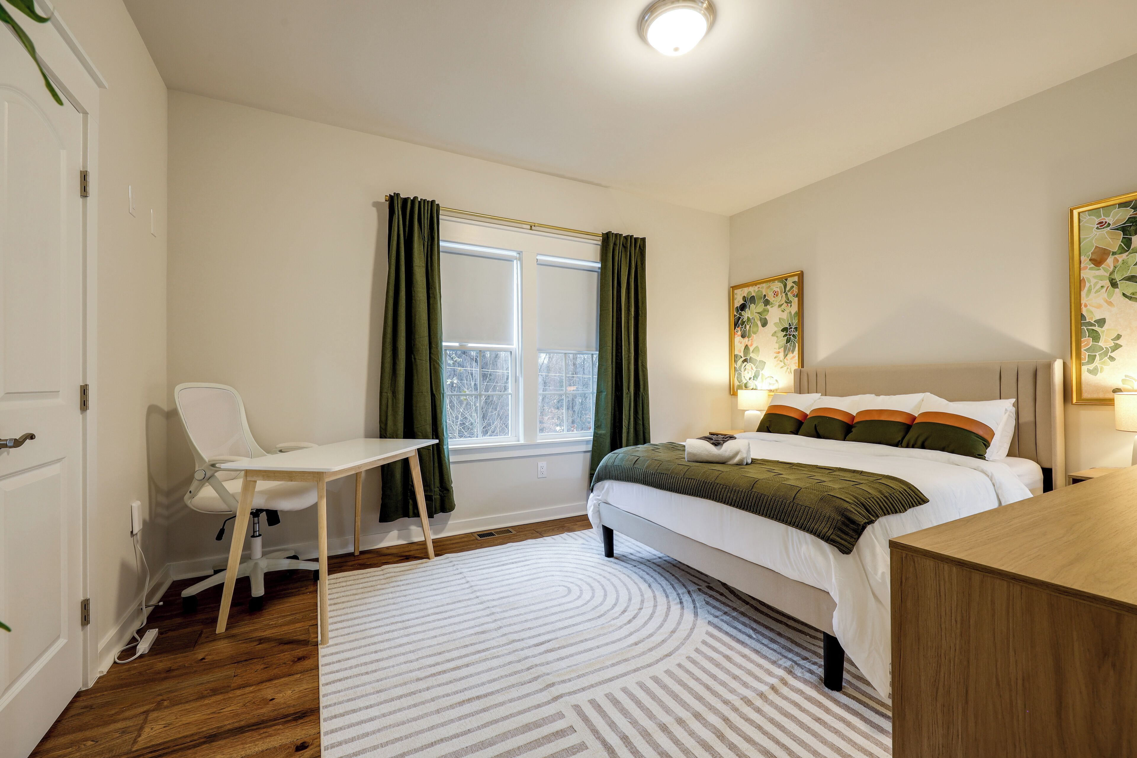 A bedroom with a bed, a desk, a chair, and a window with curtains.