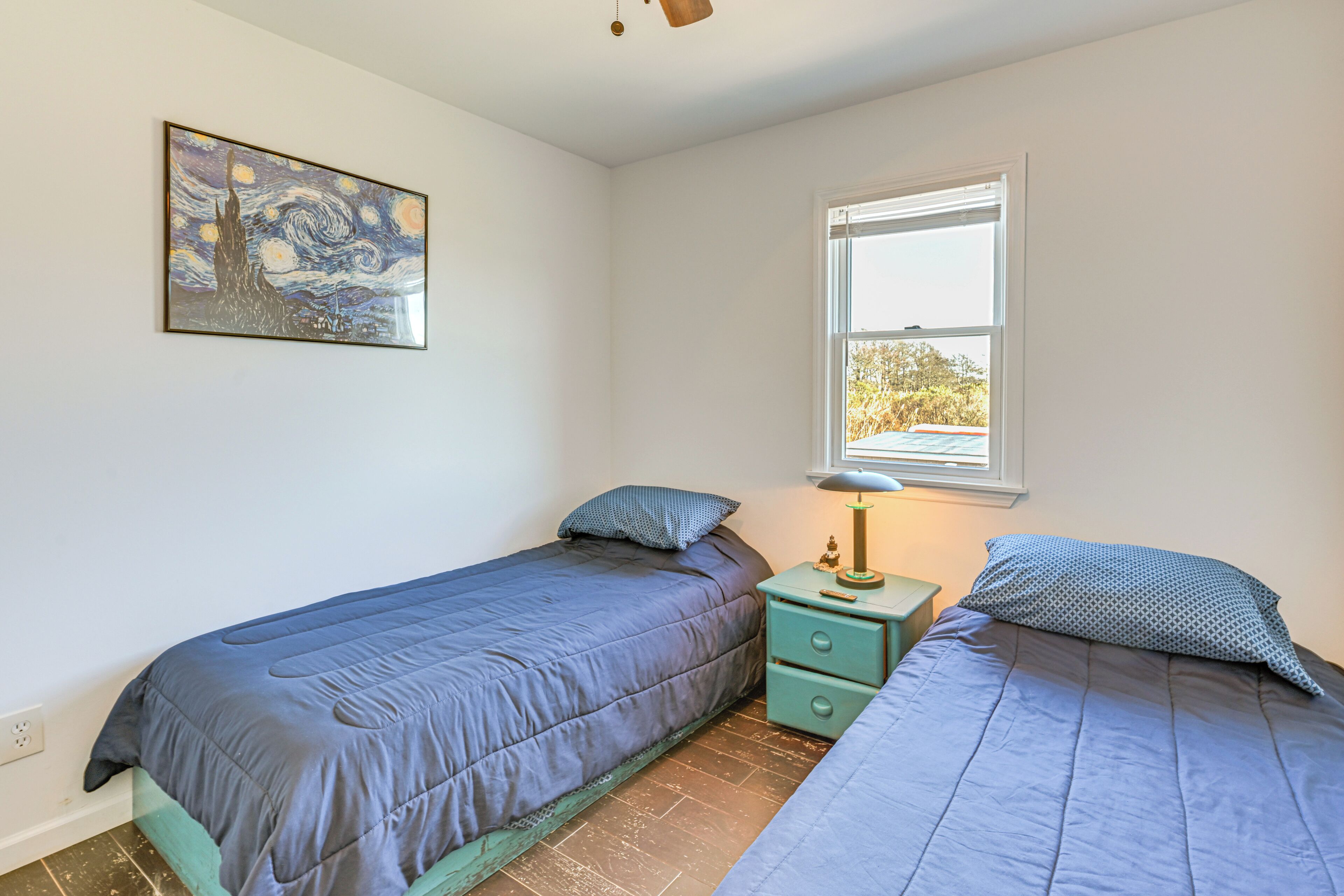 A bedroom with two beds, a nightstand, a lamp, and a window.