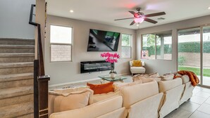 A spacious living room with a large sofa, a flat-screen TV mounted on the wall, a ceiling fan, and a staircase leading to another level. - 11 Mi to the Strip: Quiet Home in North Las Vegas (North Las Vegas)