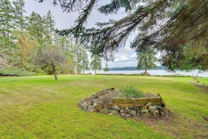 A landscaped garden with a wooden planter, a small rock garden, and a view of a lake and mountains in the background. - Beach & Bay Access! 5-acre Whidbey Island Retreat (Greenbank)