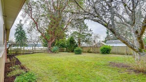 A backyard with a wooden deck, a small garden bed, and a view of a house across a fence. - Beach & Bay Access! 5-acre Whidbey Island Retreat (Greenbank)