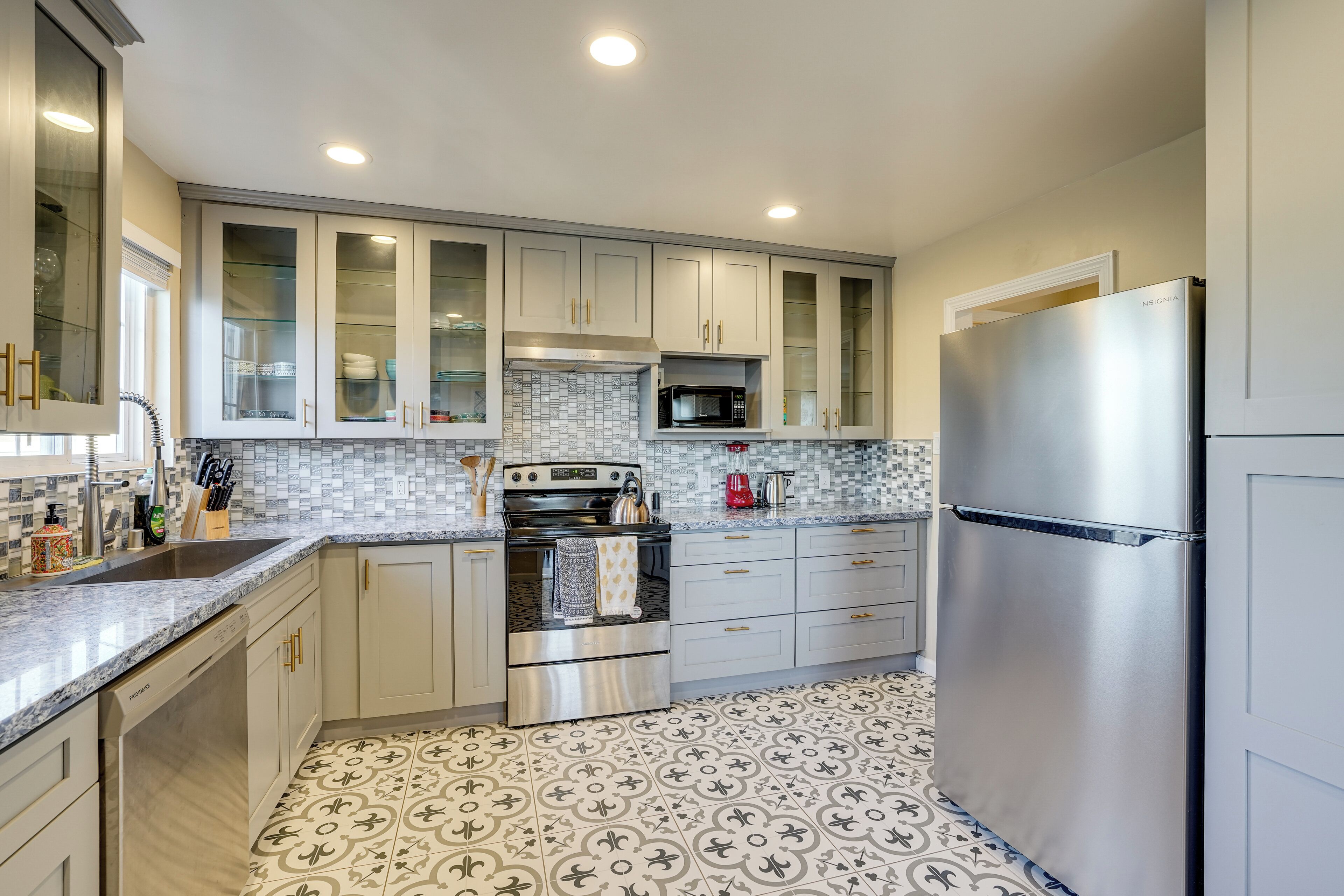 A modern kitchen with white cabinets, stainless steel appliances, and patterned floor tiles.