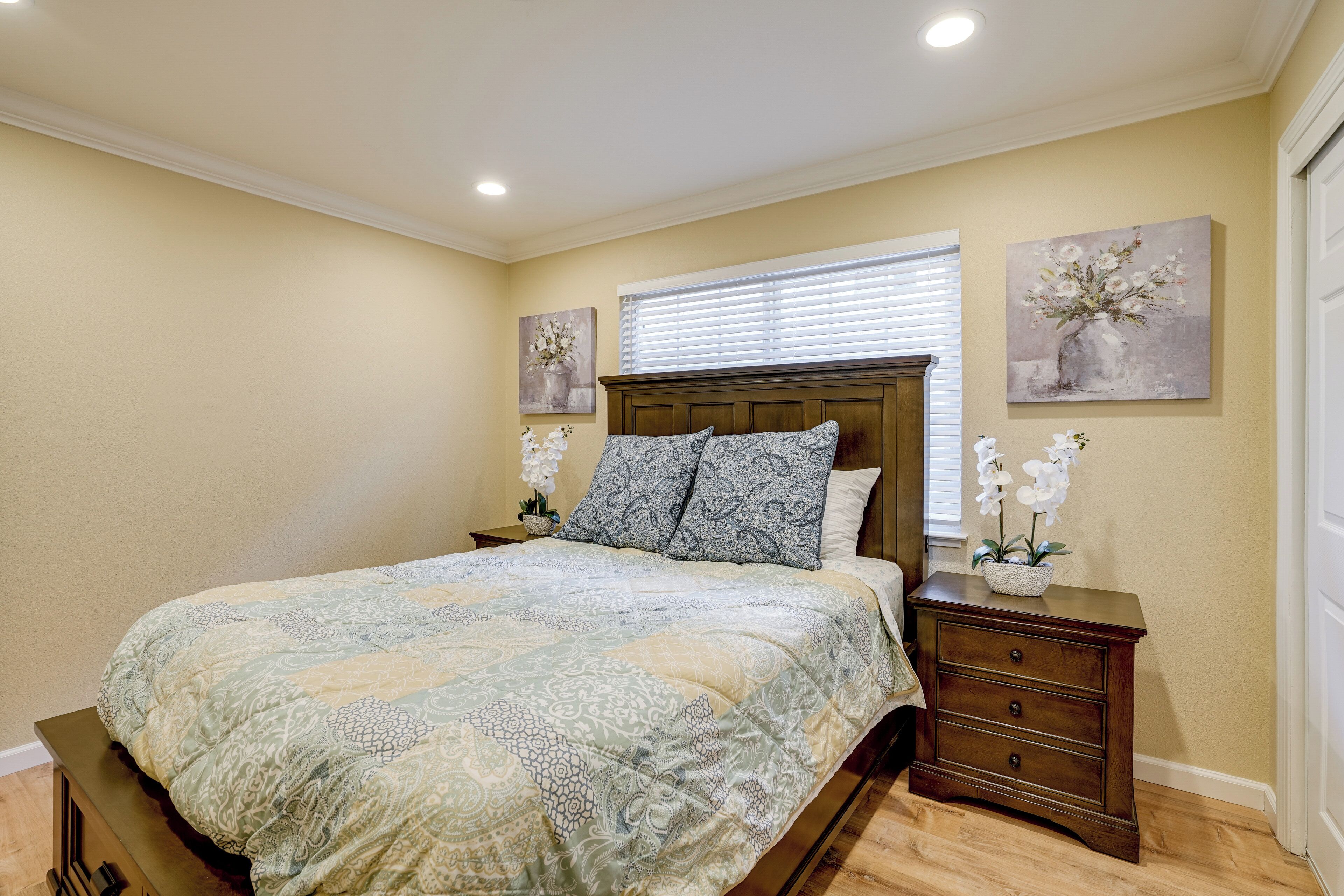 A bedroom with a bed, nightstands, and artwork on the walls.