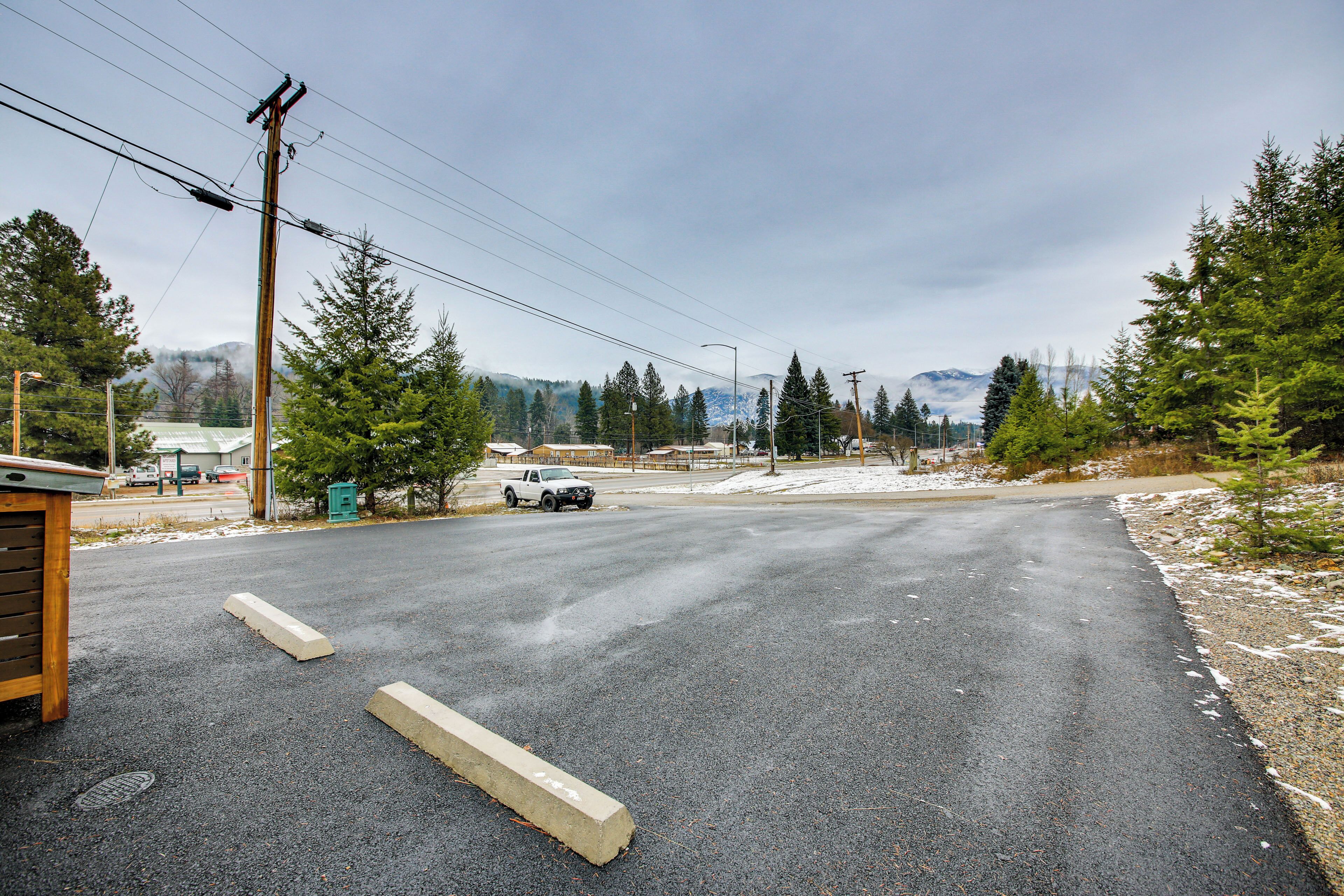 A paved road with a white pickup truck, surrounded by evergreen trees and a mountain in the background.