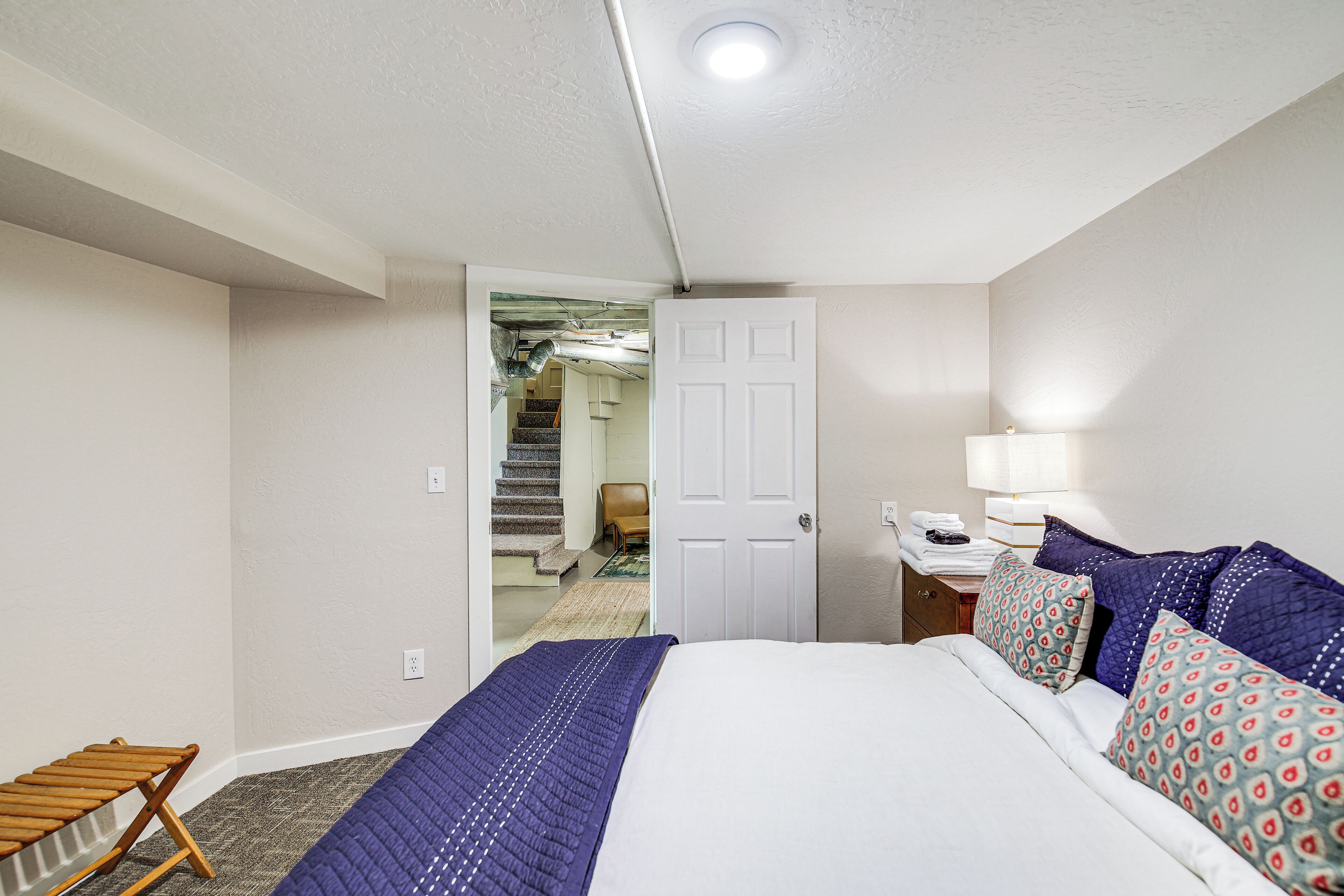 A hotel room with a bed, a chair, a desk with a lamp, and a door leading to a staircase.