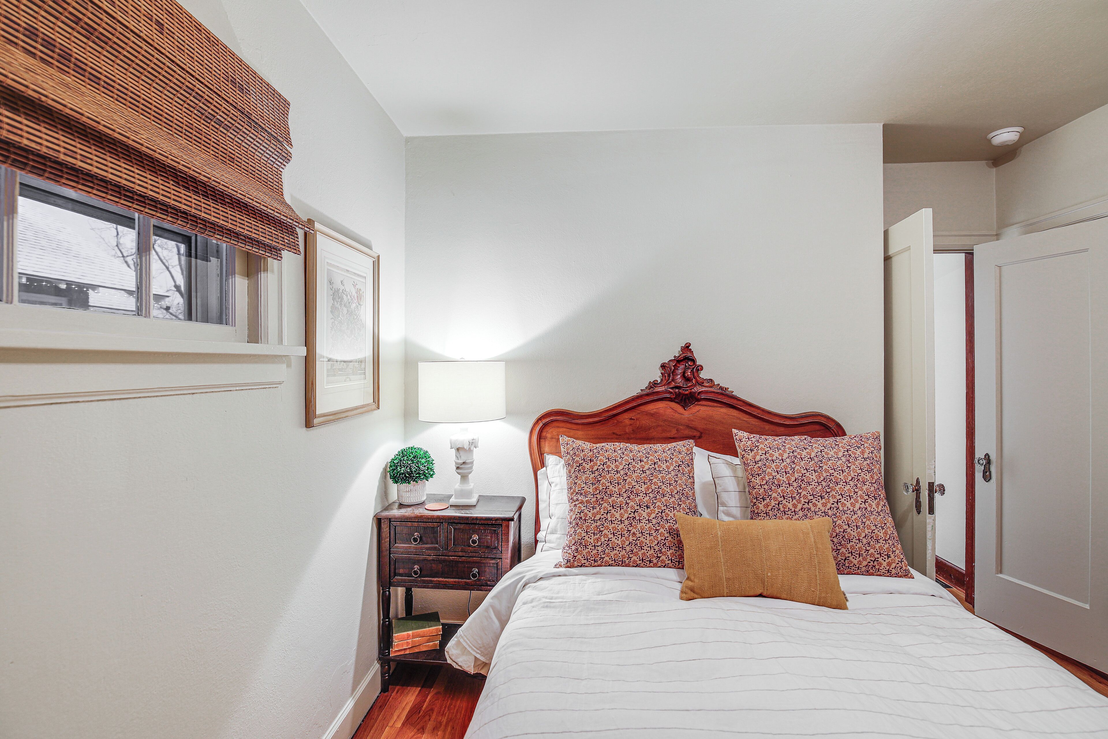 A bedroom with a wooden headboard, a bedside table with a lamp, and a window with blinds.