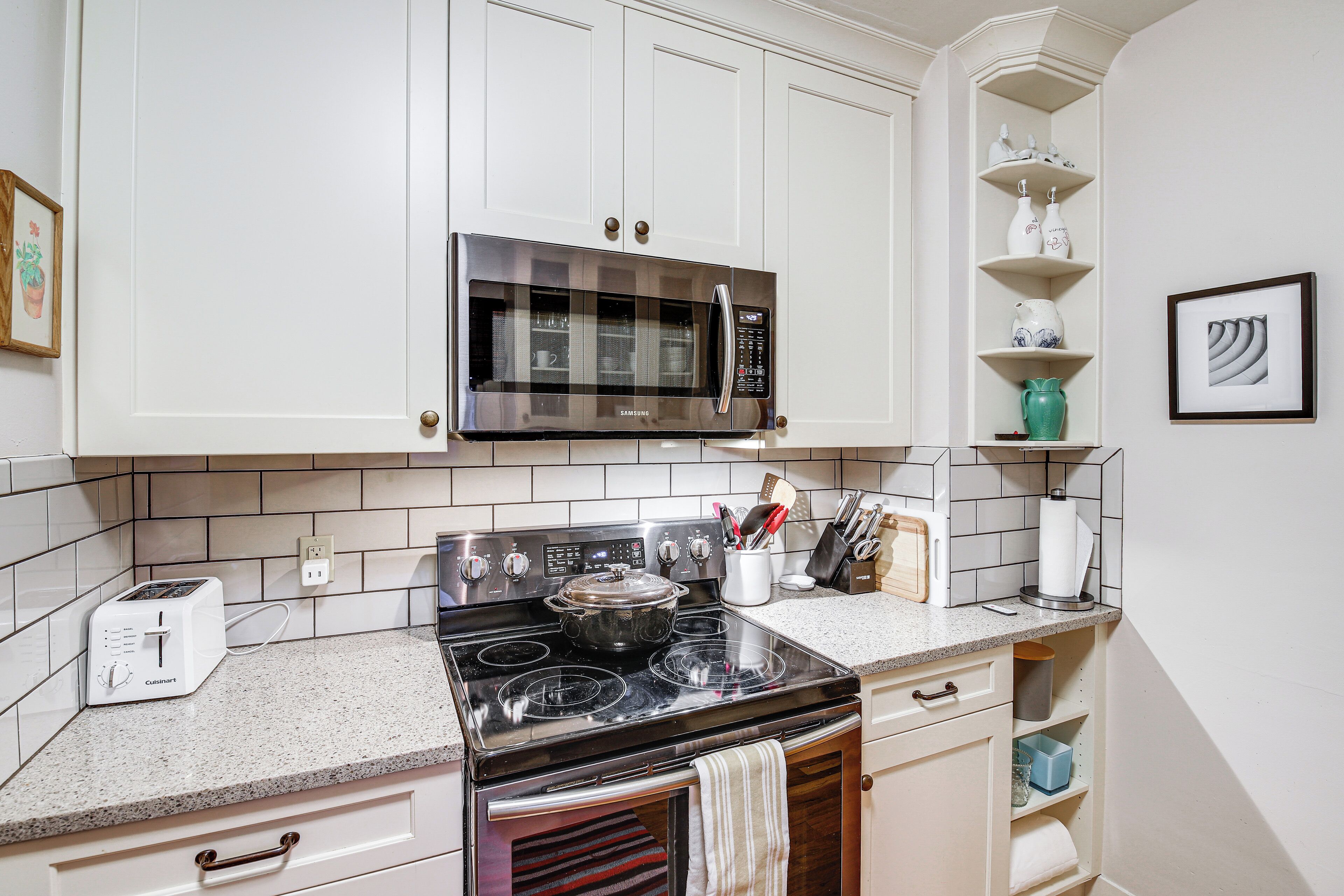 A kitchen with white cabinets, a stainless steel microwave, a black stove, and a toaster.
