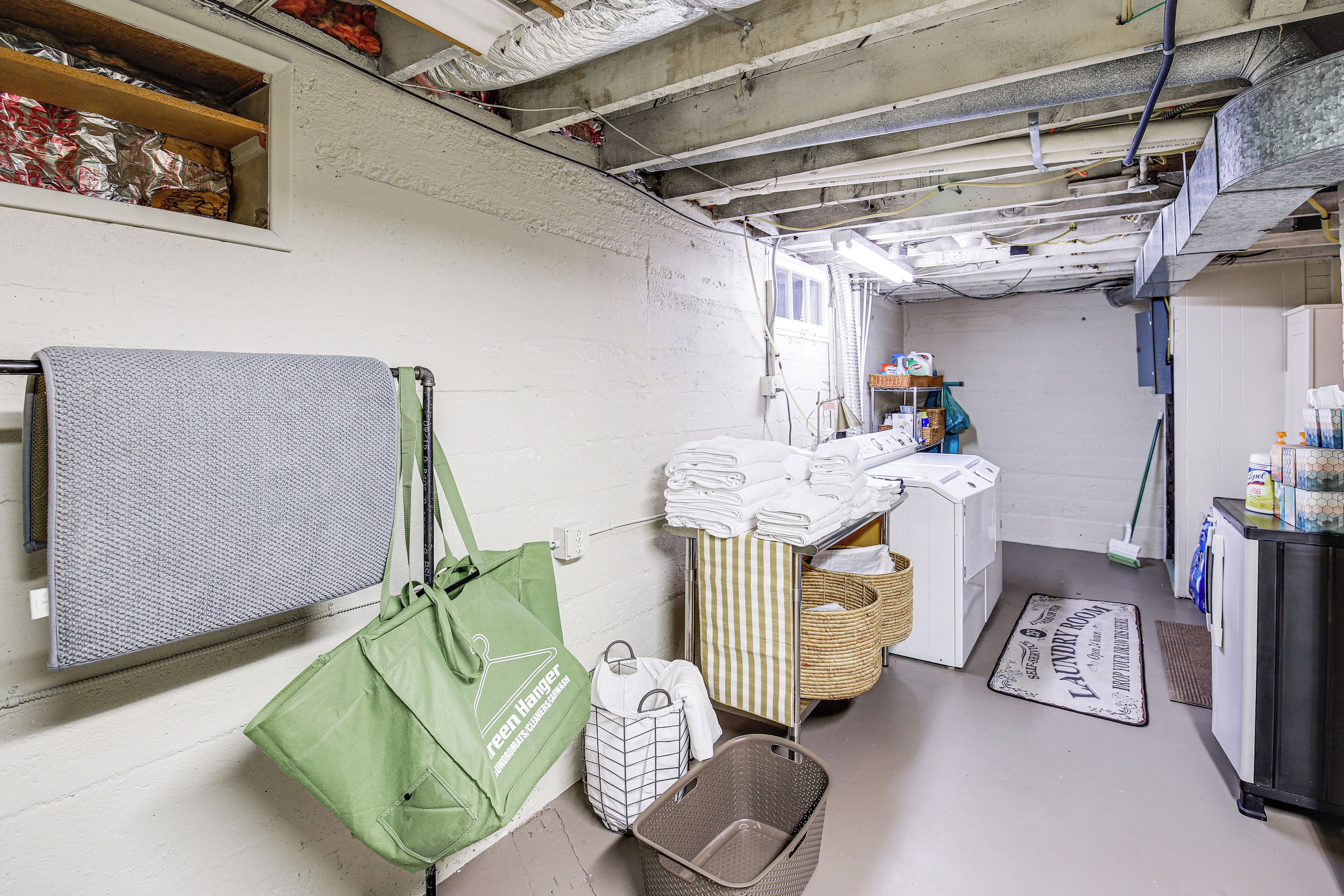 A laundry room with a washing machine, drying rack, baskets, and a green tote bag.
