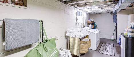 A laundry room with a washing machine, drying rack, baskets, and a green tote bag.