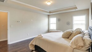 Un dormitorio con una cama grande, dos ventanas con persianas, una lámpara en el techo y un termostato en la pared.