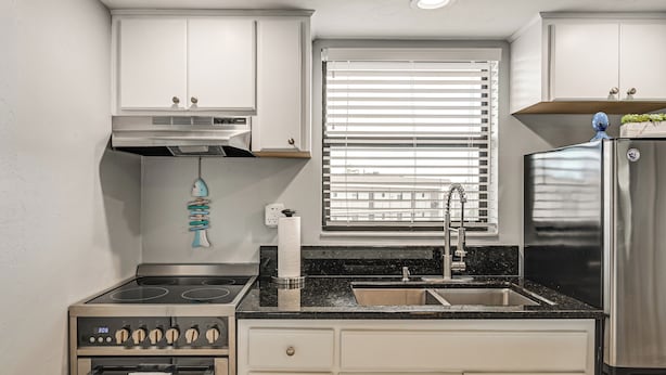 Eine moderne Küche mit weißen Schränken, einem Edelstahl-Kühlschrank, einem Backofen, einer Spüle und einem Fenster mit Jalousien.
