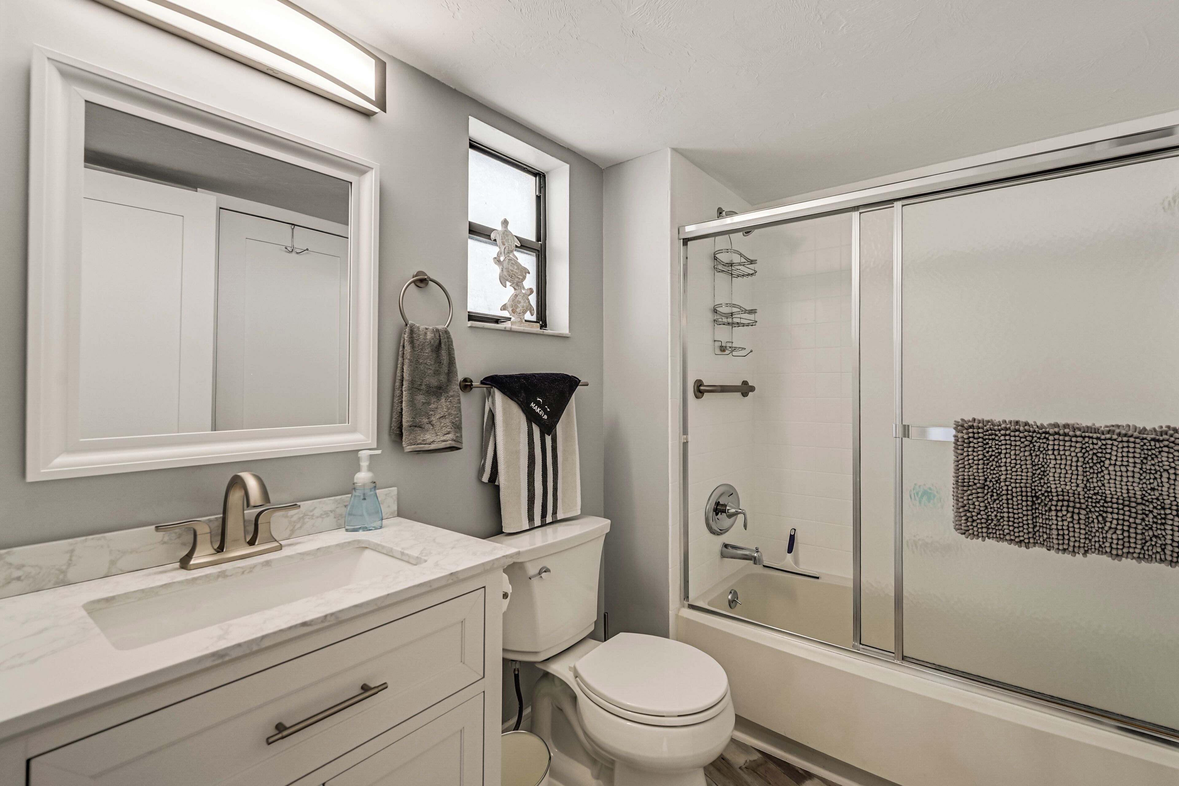 A bathroom with a sink, mirror, towel rack, toilet, and shower.