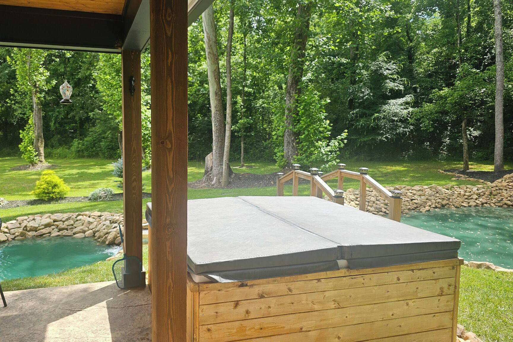 Une terrasse en bois avec un chemin de pierre menant à une piscine, le tout entouré d’arbres.