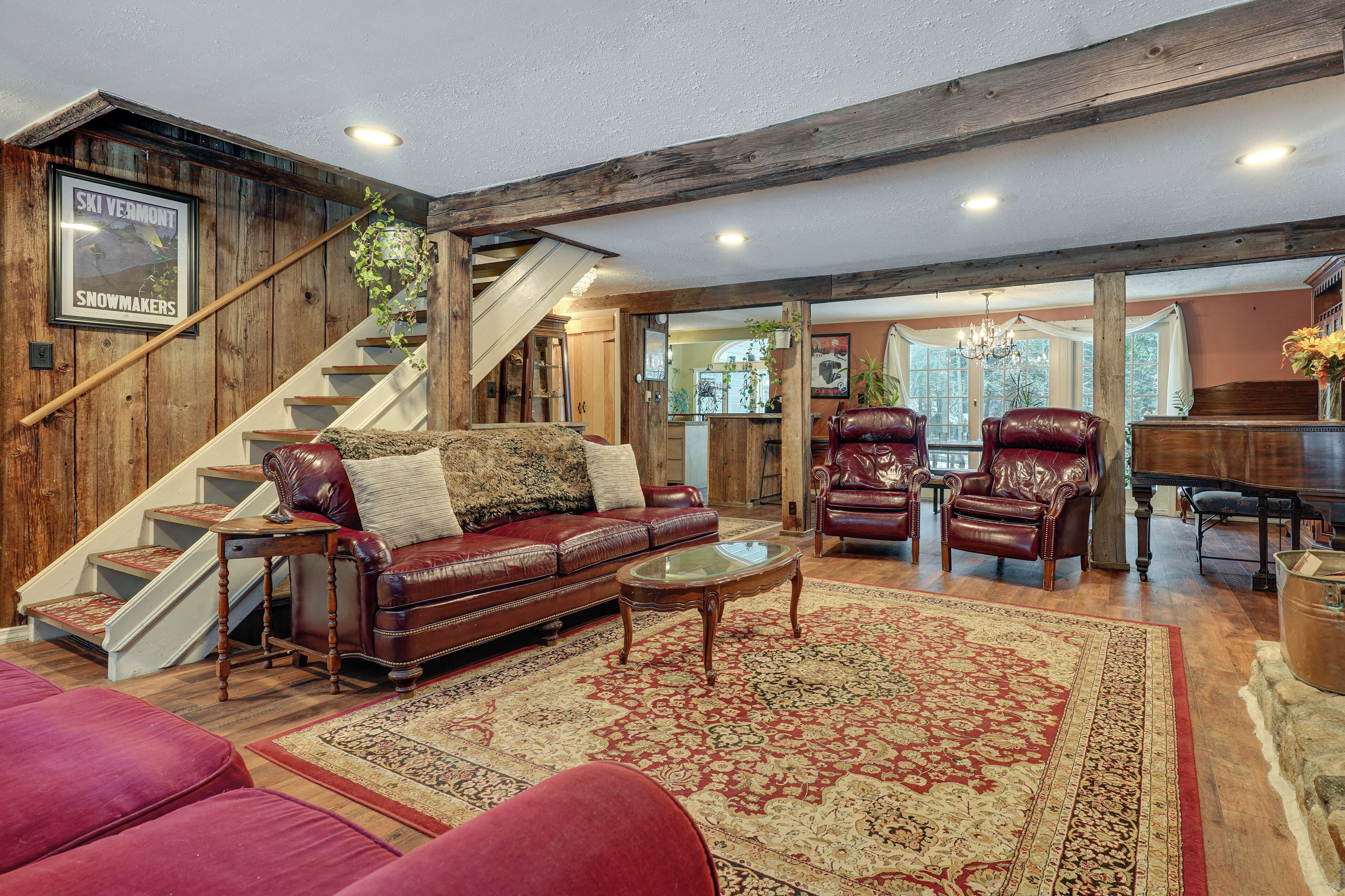 A spacious living room with a wooden staircase, leather furniture, and a large rug.
