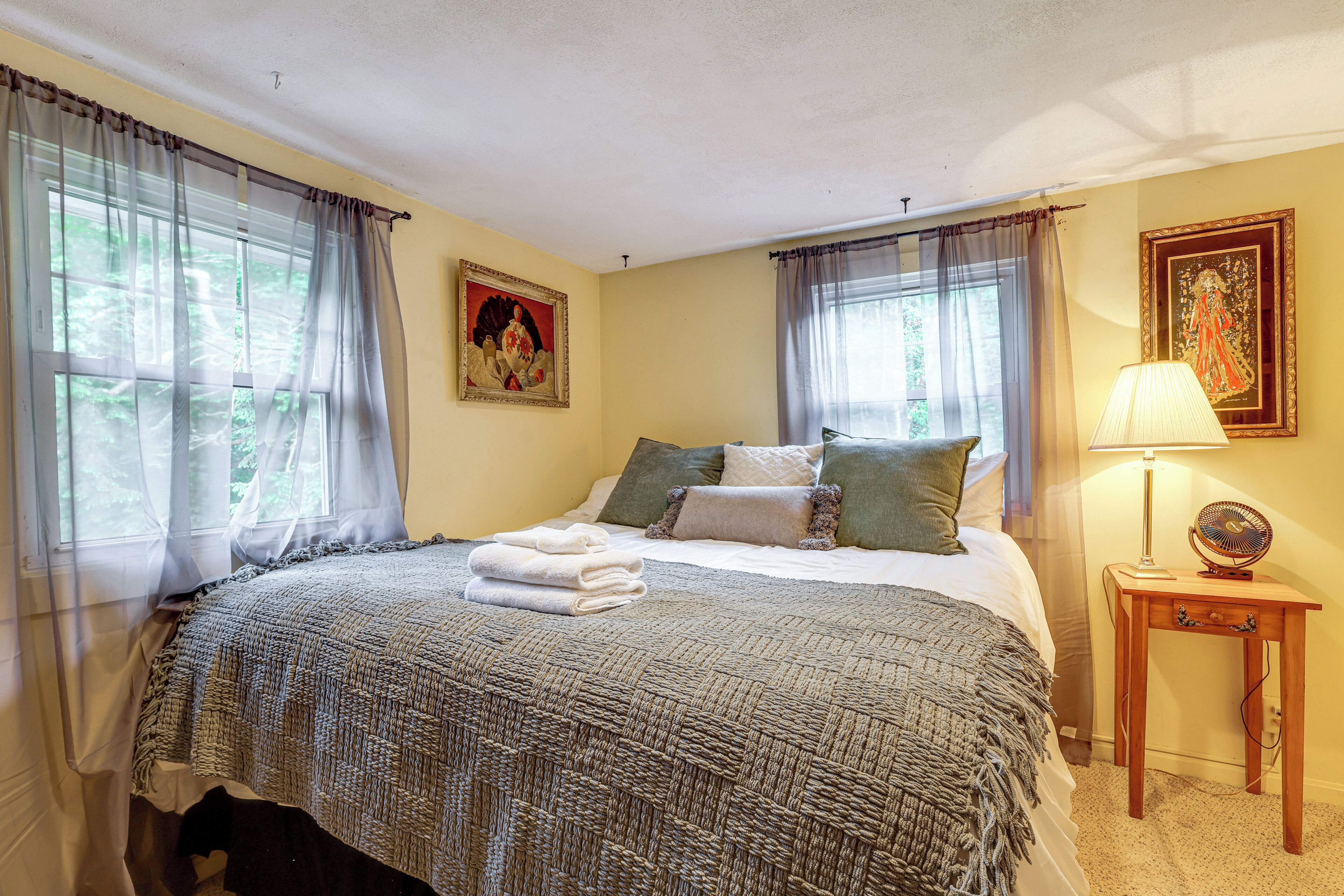 A bedroom with a bed, a bedside table with a lamp, and curtains on the windows.