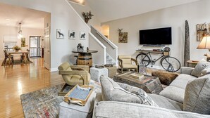 A spacious living room with a staircase, a dining area, and a television mounted on the wall. - Modern Mountain Zen 3-bed, 3-bath Home With Creeks (Sapphire)
