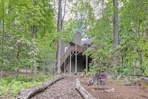 A rustic cabin with a wooden staircase leading to a covered porch, surrounded by dense forest. - Modern Mountain Zen 3-bed, 3-bath Home With Creeks (Sapphire)