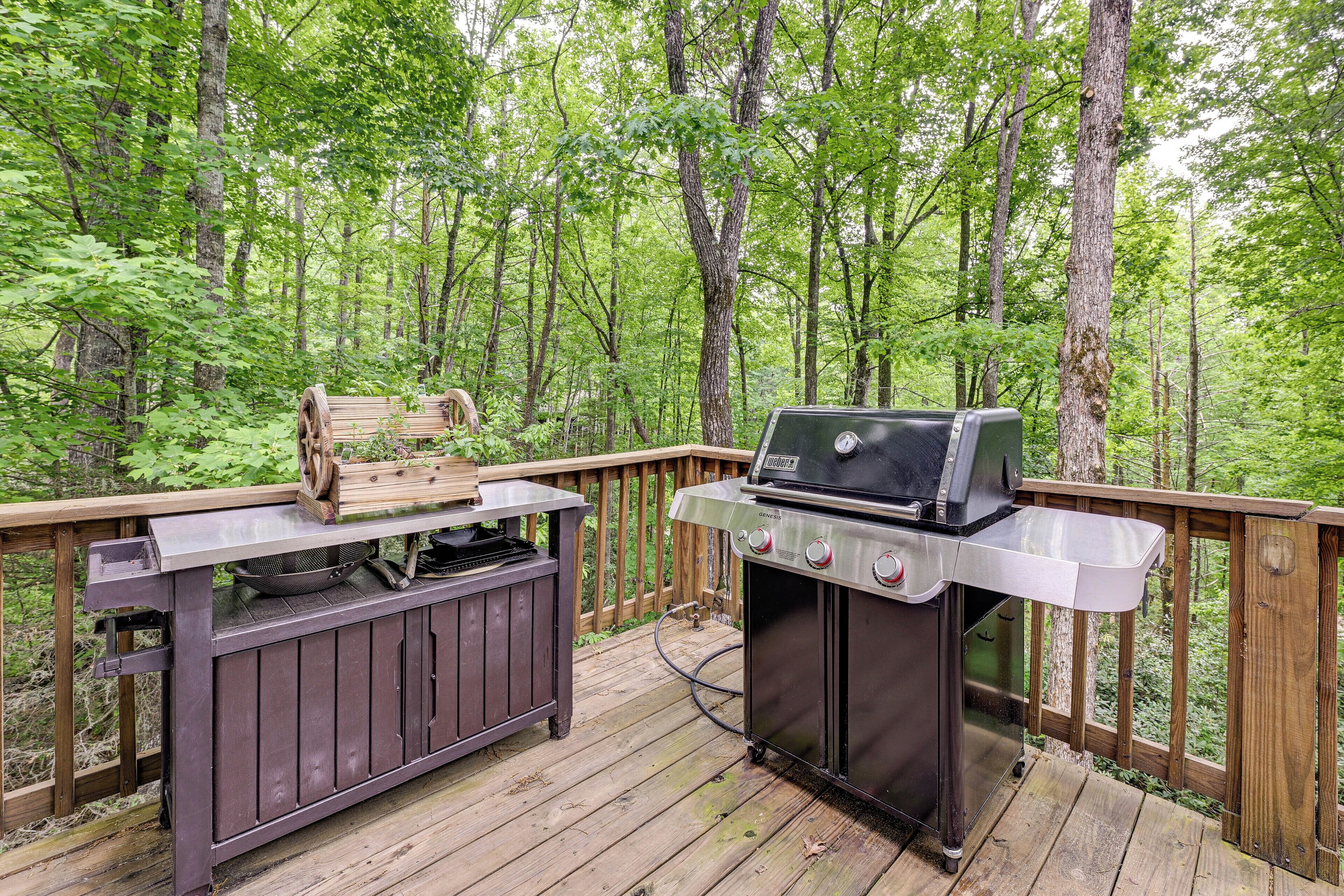 Terraza al aire libre con una parrilla y una mesa de madera, rodeada de un bosque.