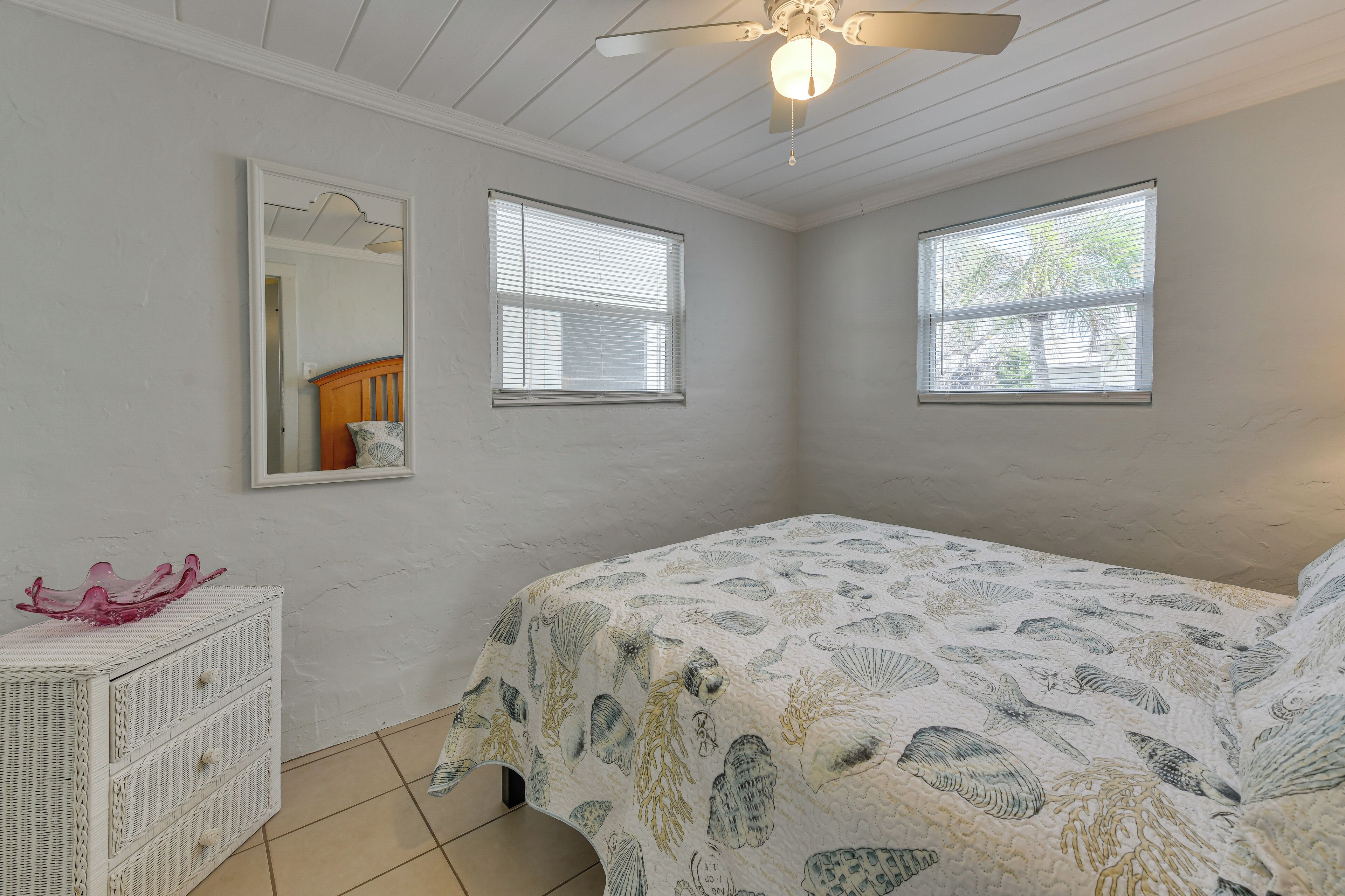 Un dormitorio con una cama, dos ventanas, un ventilador de techo y un aparador.