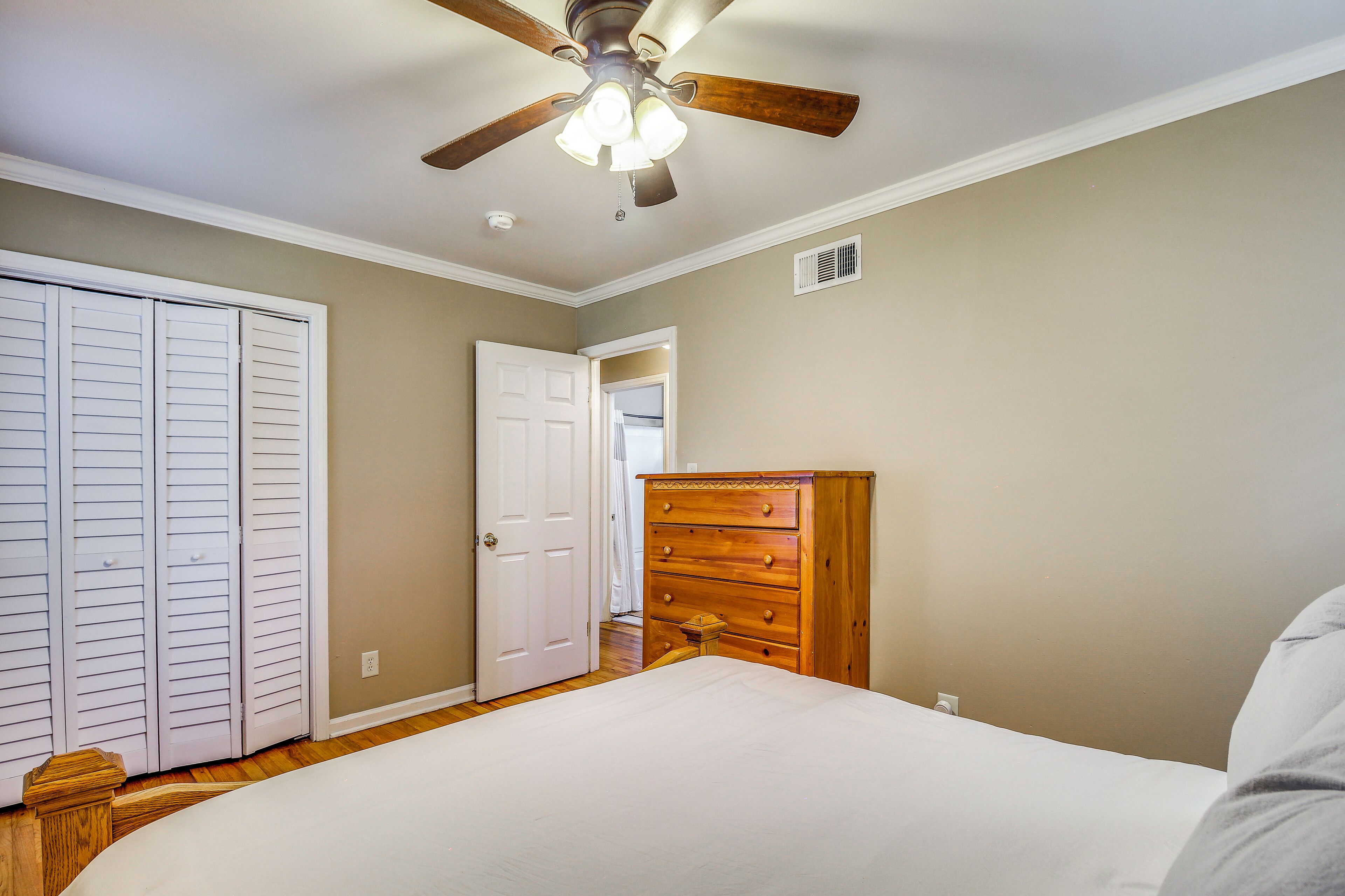 A bedroom with a bed, a wooden dresser, a ceiling fan, and a white door.