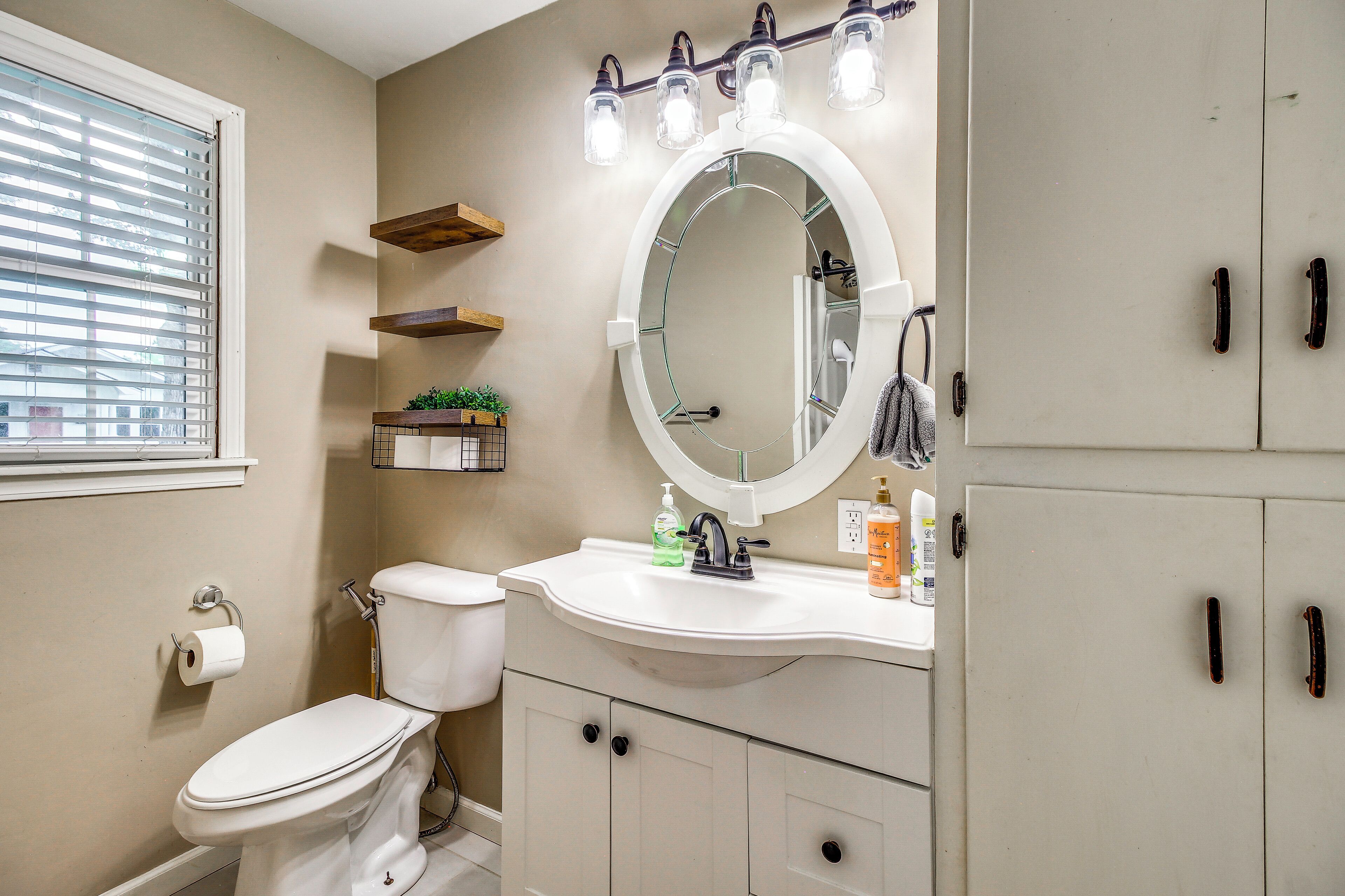 A bathroom with a toilet, sink, mirror, and storage cabinets.