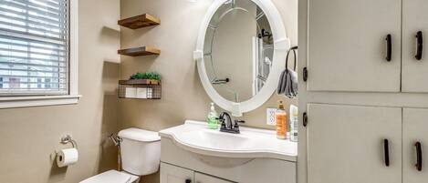 A bathroom with a toilet, sink, mirror, and storage cabinets.