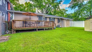 A single-story house with a deck, a fenced yard, and a large tree.