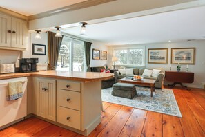 A spacious living area with a kitchen, wooden flooring, and a large window. - Hike, Fish, Hunt! Green Mountain Home By River (East Arlington)