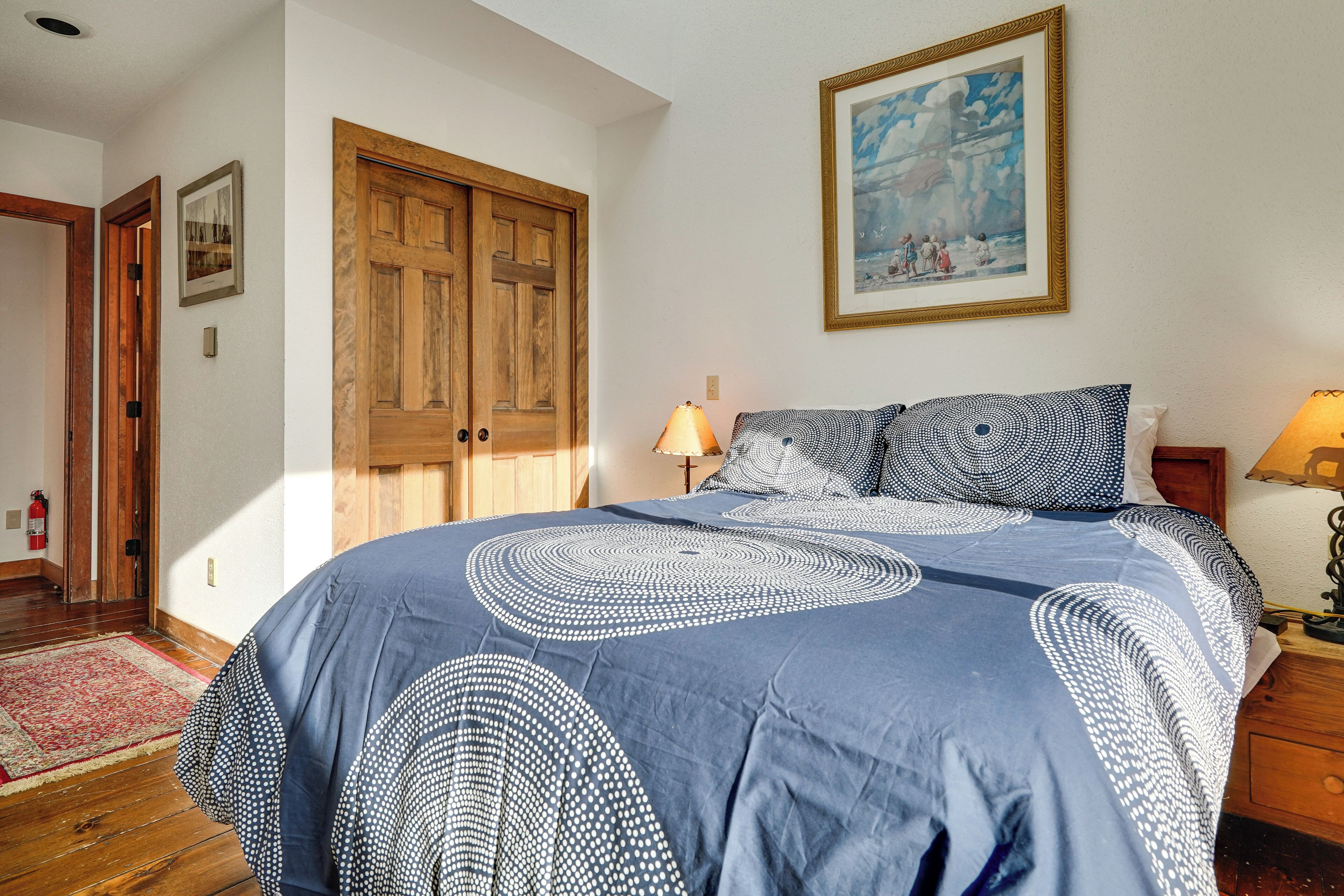 A bedroom with a large bed, wooden wardrobe, and a painting on the wall.