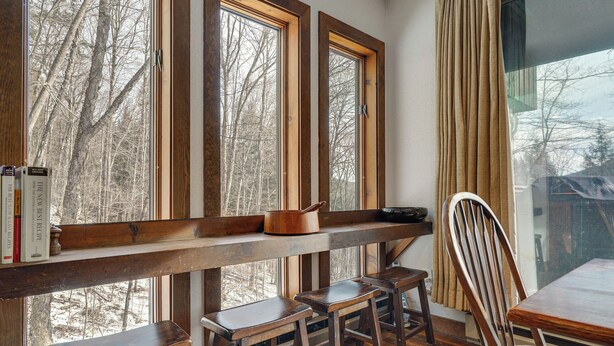 A room with a wooden bench, two stools, and a dining table with a chair. Large windows with curtains are visible. - Near Okemo & Killington: Home w/ Sauna & Fireplace (Plymouth)