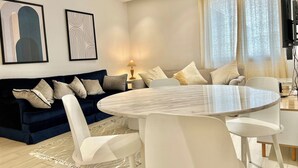 A modern living room with a round dining table, white chairs, a dark blue sofa with multiple cushions, and two abstract wall art pieces. - Light Escape at La Marsa S 24 D 11 (La Marsa)