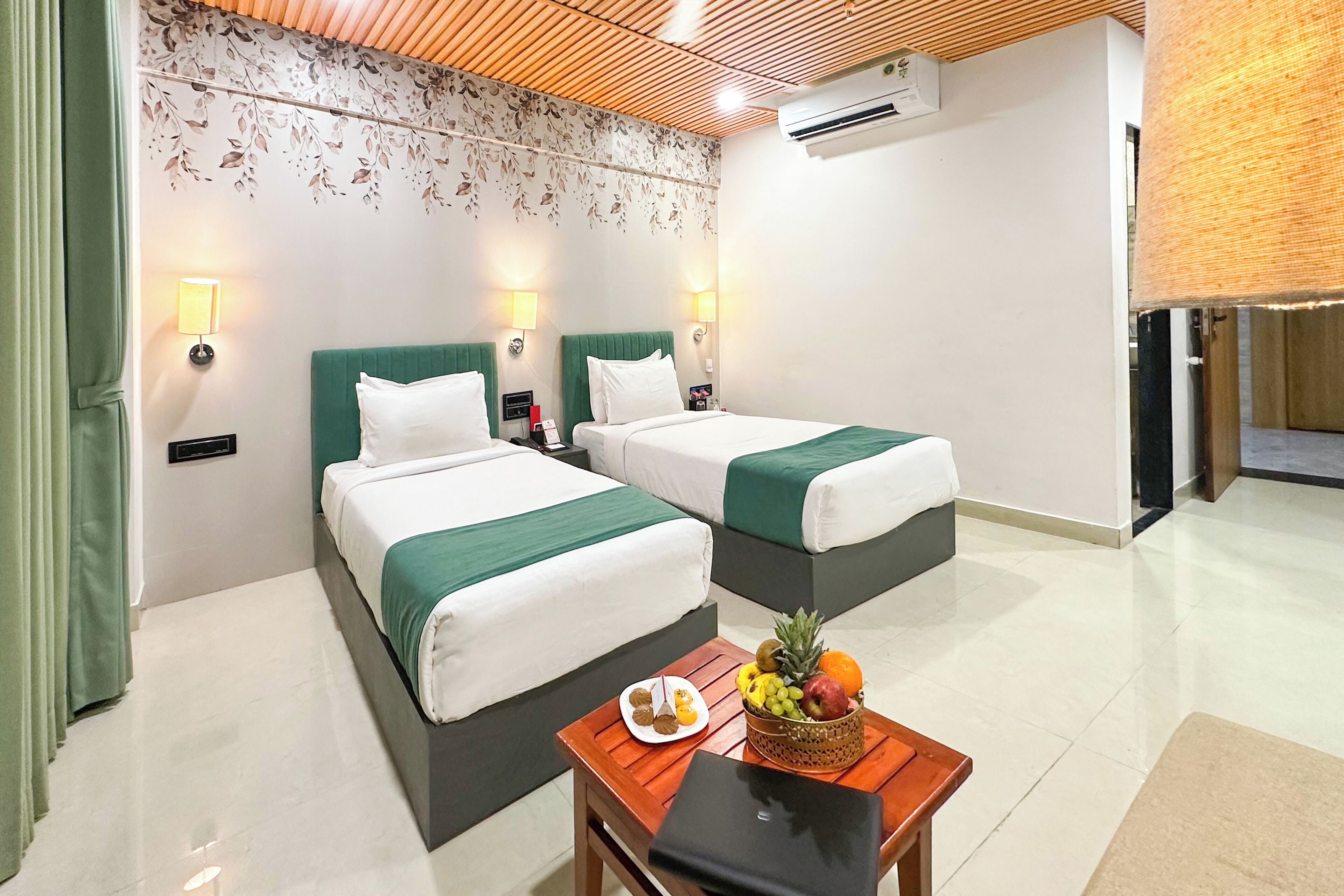 A hotel room with two beds, a small table with fruit, a laptop, and a wall-mounted air conditioner.