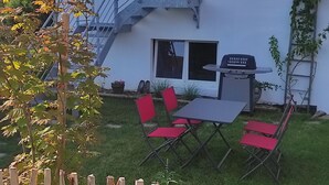 Ein zweistöckiges Haus mit Balkon, Grill und kleiner Außenbereich mit roten Stühlen.