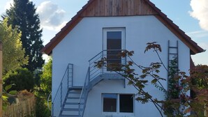 Ein zweistöckiges Haus mit Holzdach, einer Haustreppe und einem kleinen Balkon.