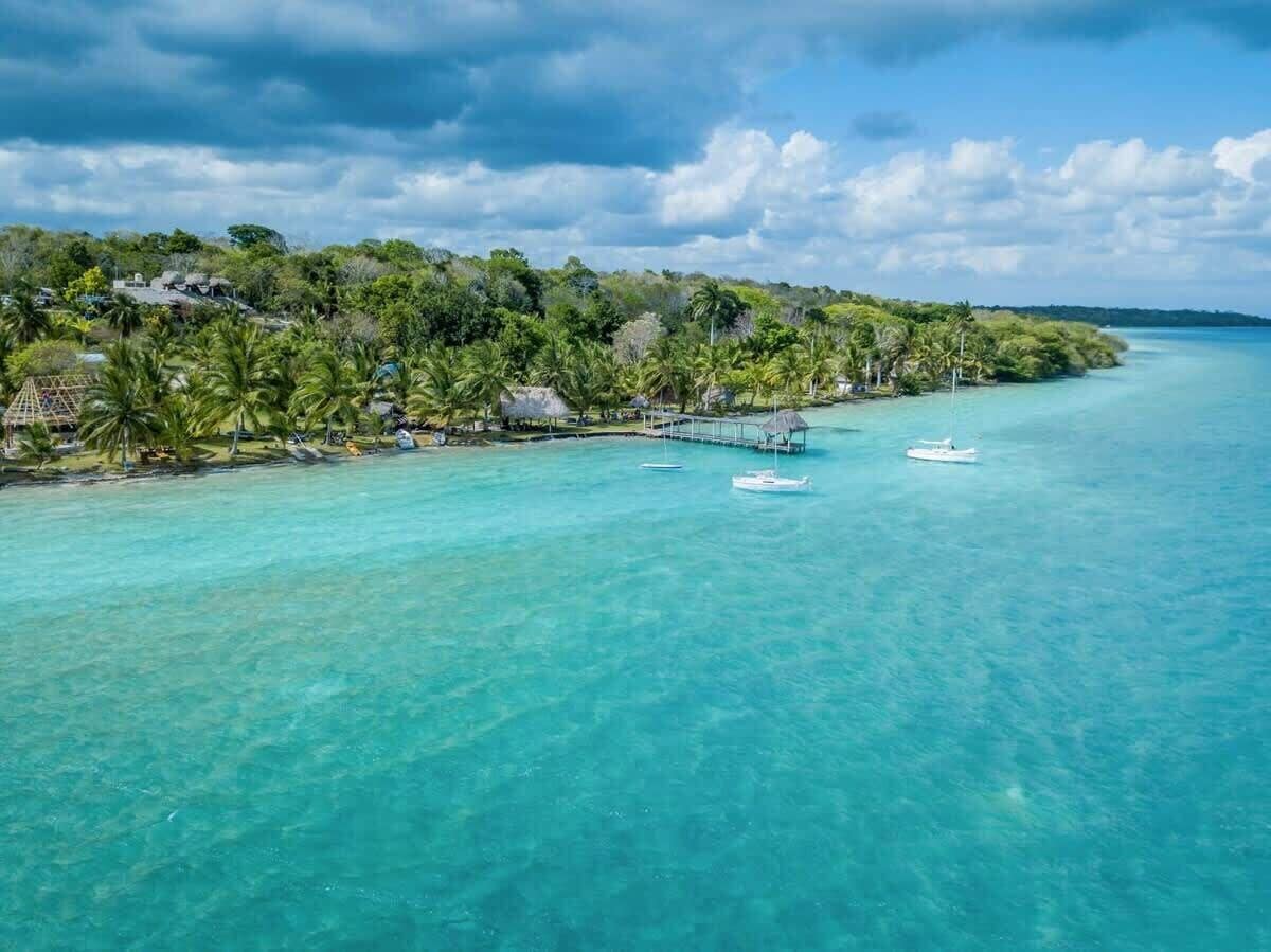 A tropical beach with clear turquoise waters, a dock, and a row of thatched-roof huts.
