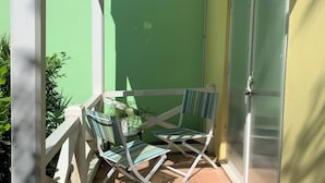 Eine Terrasse mit zwei gestreiften Liegestühlen und einem kleinen Tisch, umgeben von einem weißen Zaun und einer grünen Wand.
