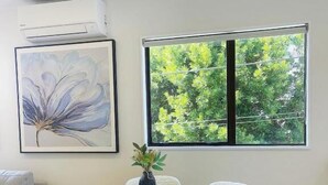 Een ronde eettafel met witte stoelen, een vaas met een plant en een lijst met kunstwerk aan de muur.