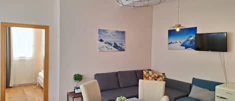 Una sala moderna con un sofá gris, una mesa de comedor con mantel de lunares y una lámpara colgante de diseño geométrico.