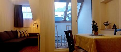 A cozy living room with a sofa, a dining table with chairs, and a view through a glass door to an outdoor area.