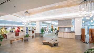 Un hall d’entrée spacieux avec un plancher en bois, un comptoir d’accueil, des espaces de détente et des luminaires modernes.