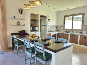 A modern kitchen with a central island, white cabinetry, and a view of a green landscape through the window.