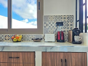 A kitchen with a window, a fruit basket, a toaster, a coffee maker, and a cup.