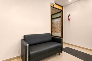 A black leather sofa in a hallway with a fire extinguisher mounted on the wall. - Hotel O Ambuja City Centre Mall (Raipur)