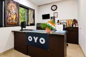 Una oficina con un mostrador de recepción identificado con 'OYO', una computadora, una planta y un reloj de pared.