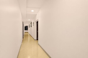 Un pasillo largo y estrecho con paredes blancas y un suelo brillante, que conduce a una puerta al final.