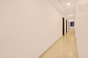 A long, narrow hallway with white walls and a tiled floor. - Hotel O Ambuja City Centre Mall (Raipur)