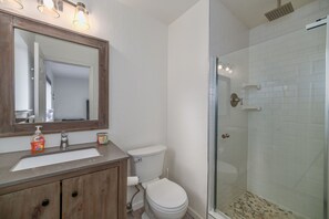 A bathroom with a wooden vanity, a white toilet, a glass shower enclosure, and a large mirror. - The Azure Tahoe Cabin 3 Bedroom Home (South Lake Tahoe)