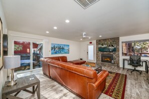 A living room with a leather sofa, a fireplace, and a stone wall. - The Azure Tahoe Cabin 3 Bedroom Home (South Lake Tahoe)