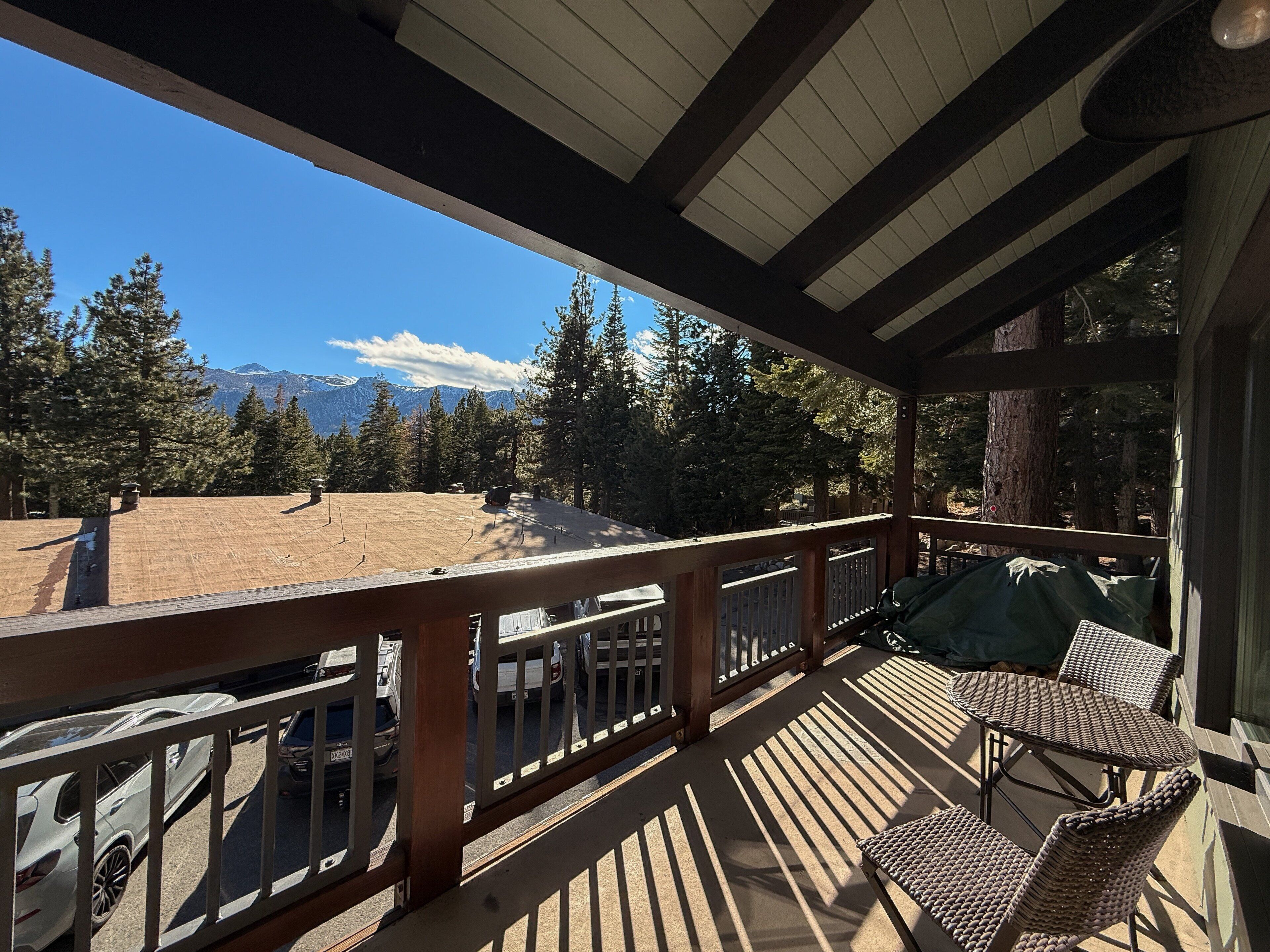 A covered outdoor area with a wooden deck, a table and chairs, and a view of a mountainous landscape.