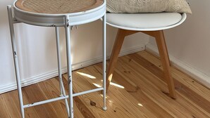 A round white metal table with a woven seat, a white cushioned chair with a patterned cushion, and a wooden floor. - Charming half-timbered house in the heart of the city "Fachwerkstube" 3 Bedroom Apartment (Witzenhausen)